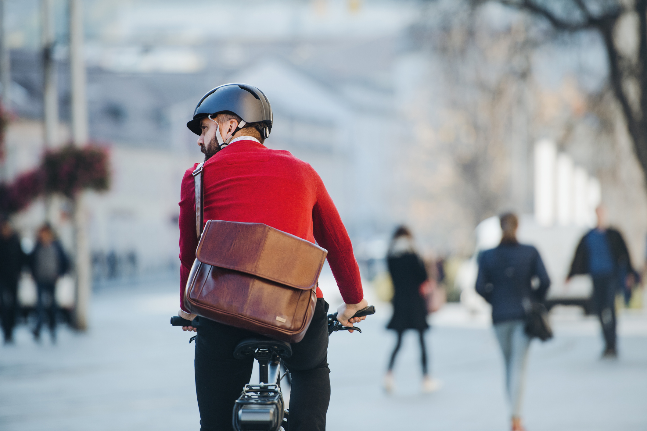 A rear view of businessman commuter with electric bicycle traveling to work in city.